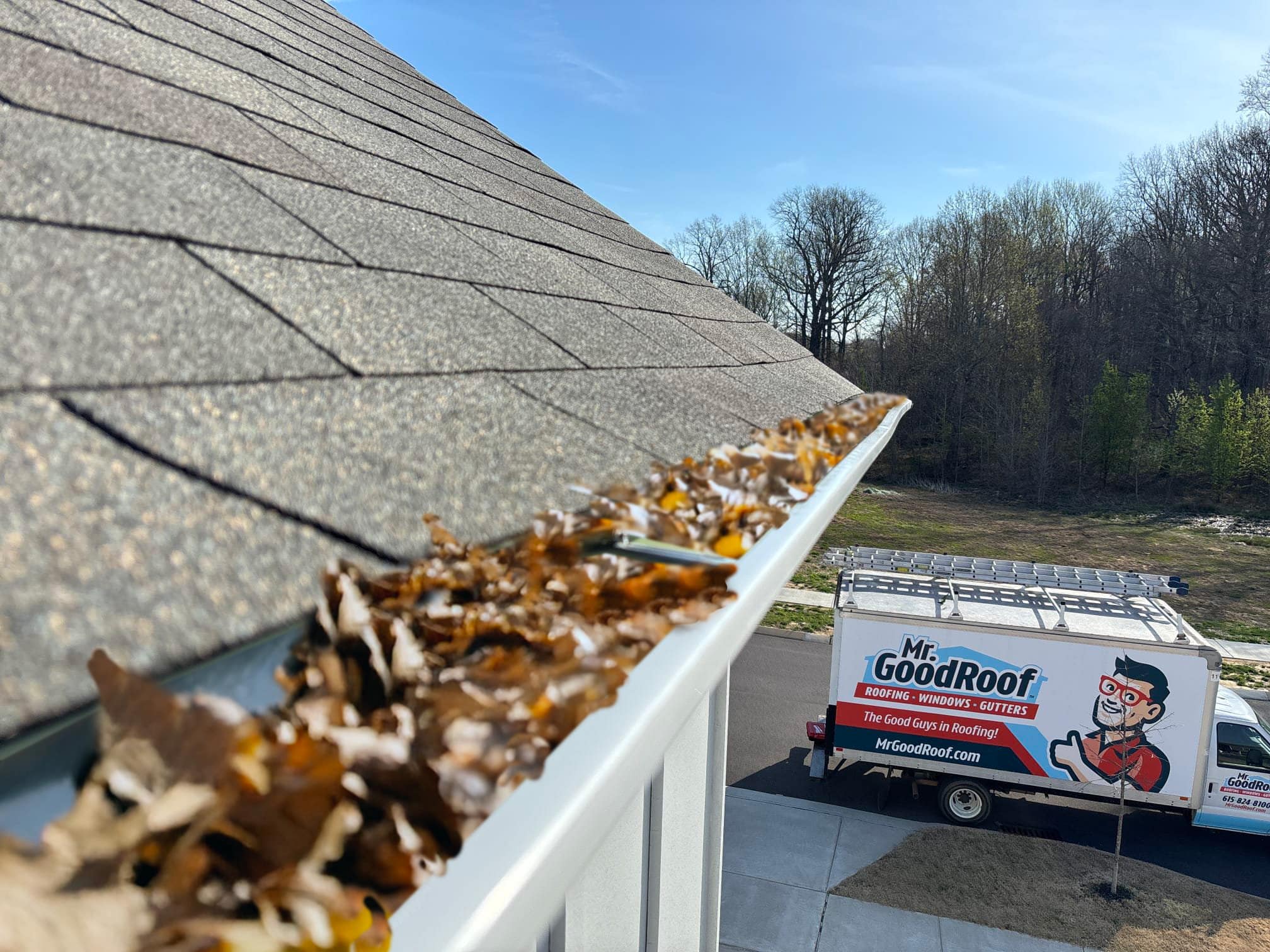 Leaf-filled gutter with a Mr. GoodRoof service truck below the roofline.