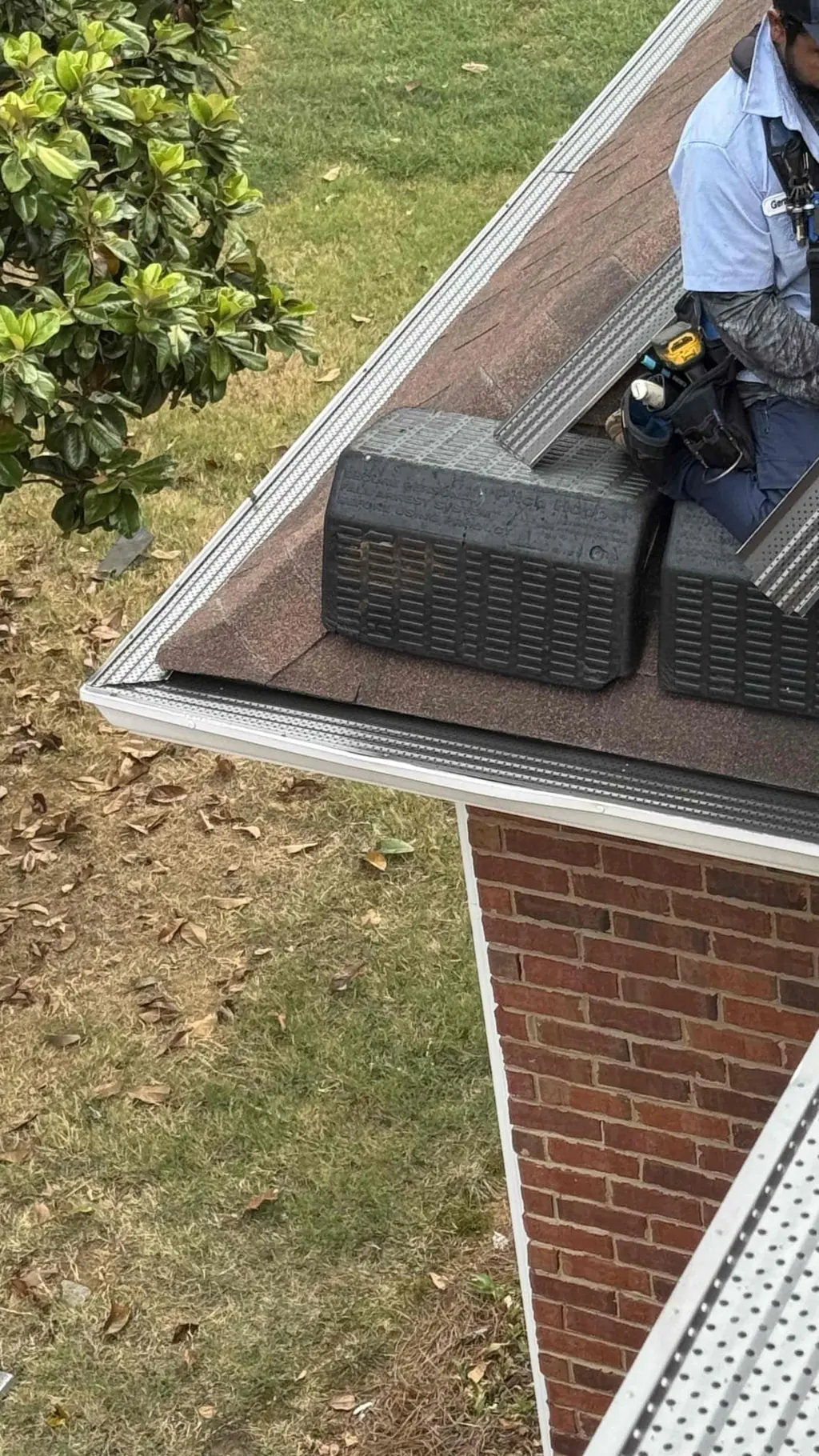 Installer working beside the gutter screen and brown shingles at the roof edge.