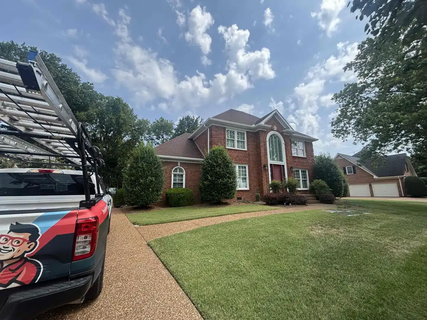 Mr. GoodRoof truck beside the brick home featured in this Hendersonville roofing project.