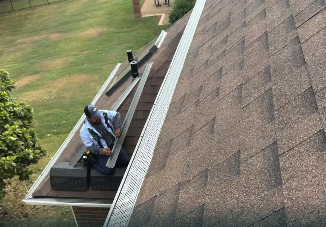 A technician working with gutter guard sections beside a shingle roof.